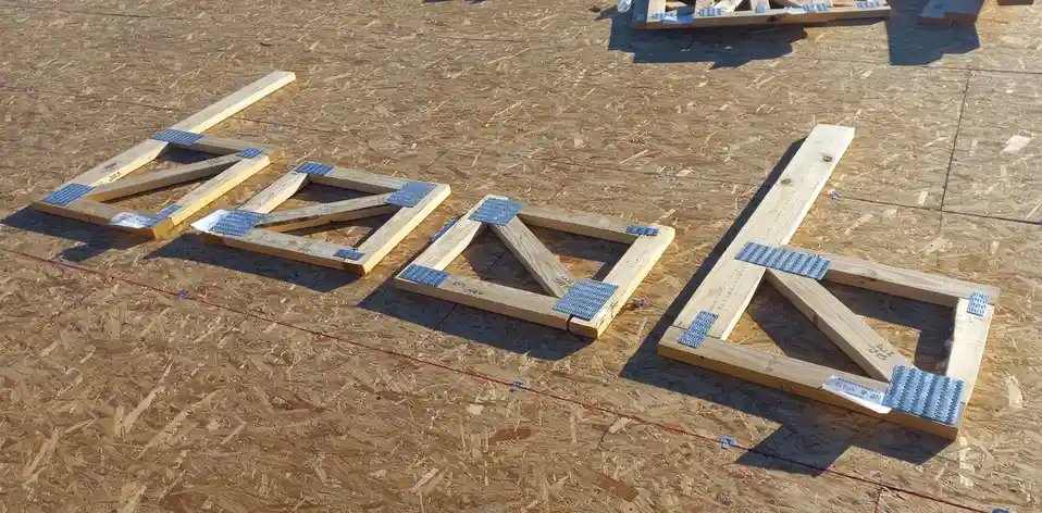 Four large wooden letters spelling 'DUD' lie on a construction site floor made of oriented strand board. Each letter is…