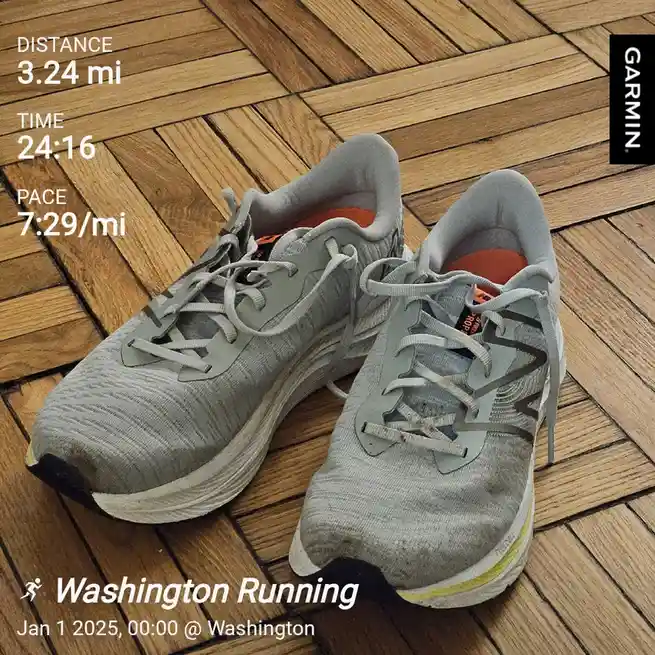 A pair of worn grey running shoes sits on a wooden floor, overlaid with a Garmin fitness tracker screenshot showing a…