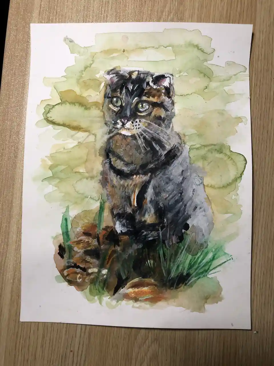 A watercolor painting on paper depicts a cat with dark, wild-looking fur and intense green eyes, sitting amidst green grass…