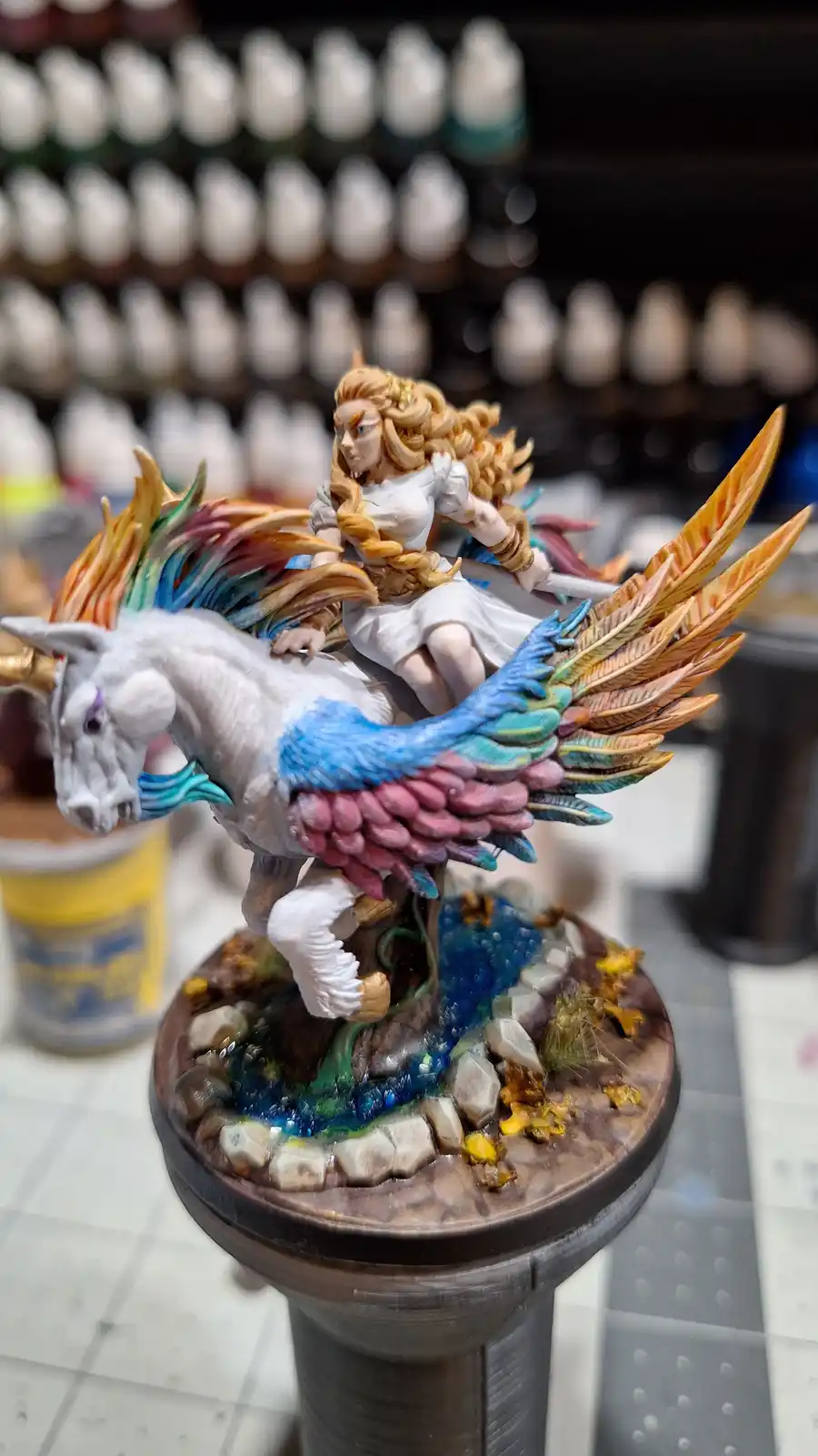 A highly detailed, hand-painted miniature figurine shows a female warrior with long blonde hair riding a white unicorn that…
