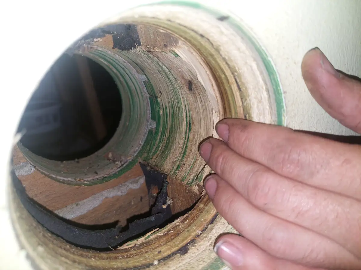 A close-up photo shows a hand holding a severely damaged, layered wooden object with peeling green paint, exposed wood…