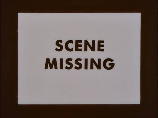 A white sign with bold, brown, uppercase text reading 'SCENE MISSING' is centered on a dark brown background. The text is…