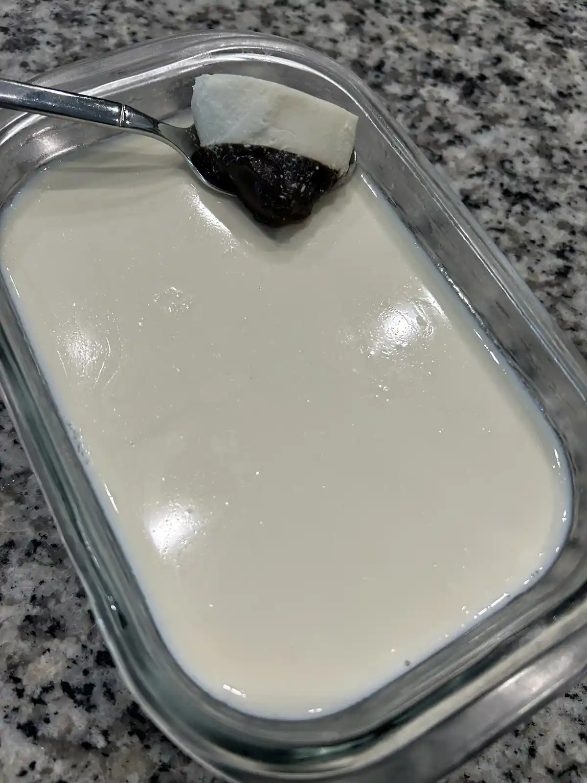 A close-up photo shows a spoon holding a scoop of white, creamy substance layered with a dark, viscous, almost black…
