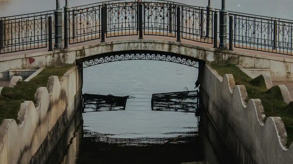 Vibrant city bridge stretches across the canal, its stone arches reflected in the rippling water below. Street lamps cast a…